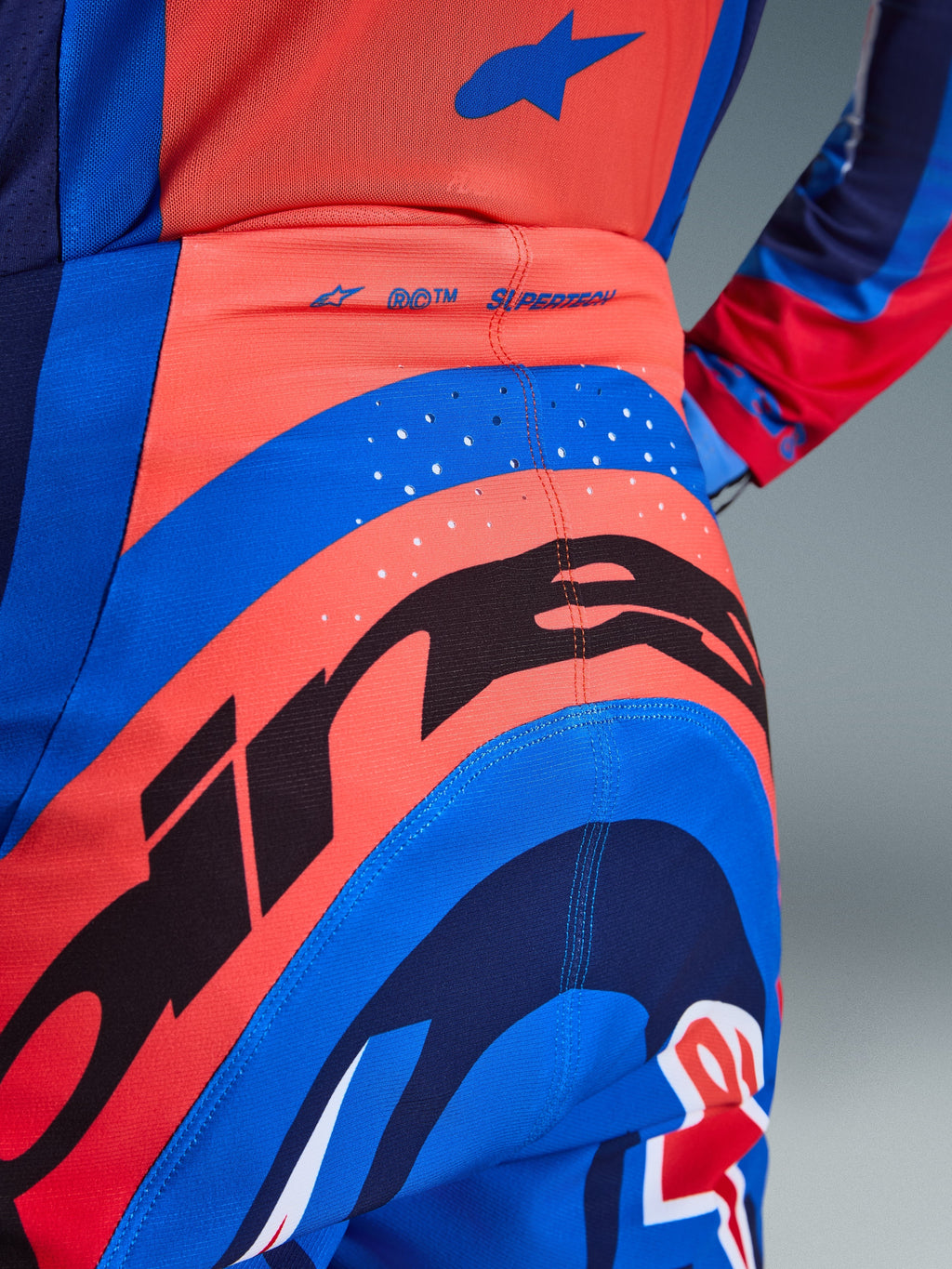 Pantalon Alpinestars Supertech Vista 2026, pantalon de motocross, bleu marine foncé, corail vif et cobalt, vue arrière rapprochée montrant un marquage audacieux, des perforations découpées au laser pour la ventilation et le logo « SUPERTECH » sur la taille, matériau extensible haute performance pour la course tout-terrain