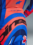 Gros plan sur le pantalon Alpinestars Supertech Vista 2026, pantalon de motocross, Hot Coral et Bleu Cobalt, avec un grand graphique Alpinestars noir sur l'assise, des perforations de ventilation découpées au laser et le marquage « SUPERTECH » à l'arrière de la taille, équipement de course professionnel