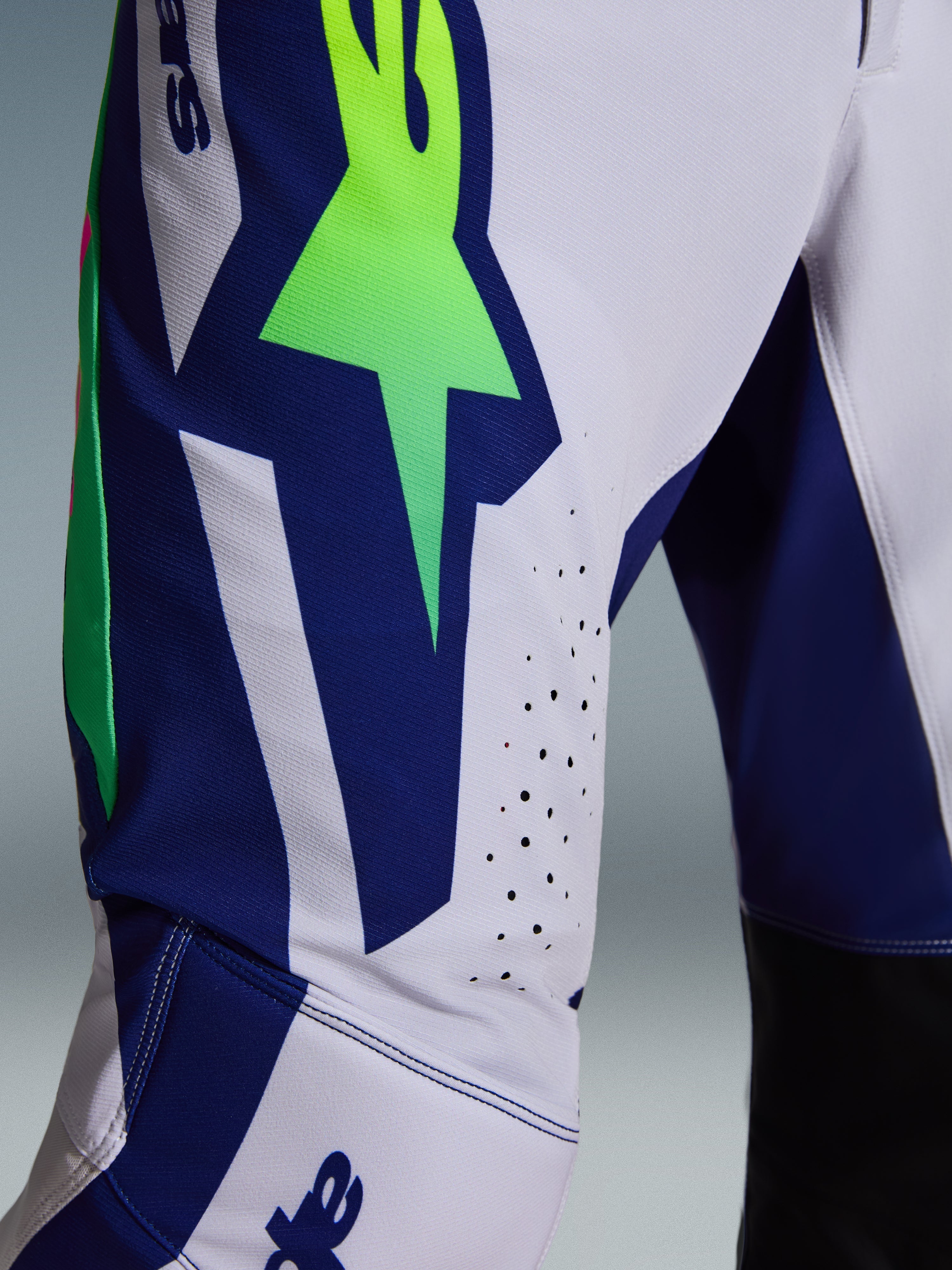 Alpinestars 2026 Supertech Vista Pants, Motocross Pants, Light Gray Yellow Fluo and Blue, close-up detail of the thigh and knee area featuring a bold neon green star logo on a blue panel, laser-cut perforations for ventilation, and black inner knee panels.