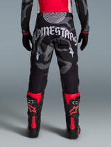 Pantalon Alpinestars Techstar Beast Coast Édition Limitée, camouflage gris et noir, lettrage blanc au dos et bottes rouges.