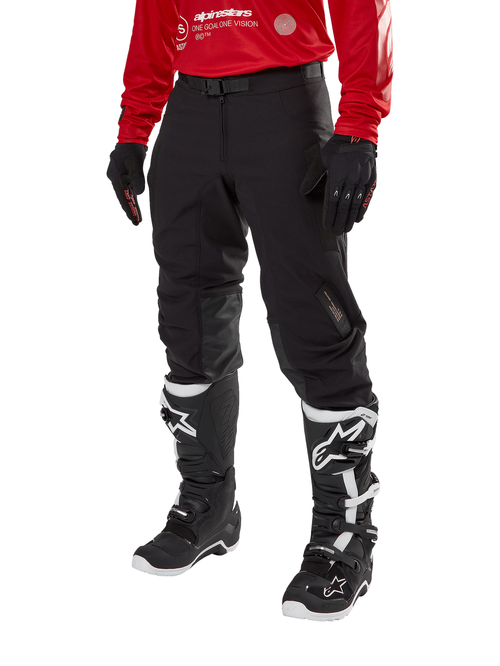 Alpinestars Techdura Pants, pantalon de moto tout-terrain noir, porté avec un maillot rouge à manches longues et des bottes de motocross noires et blanches, doté d'une construction robuste en polyamide extensible, de renforts de genoux internes en cuir et d'une ceinture à boucle réglable pour l'enduro.