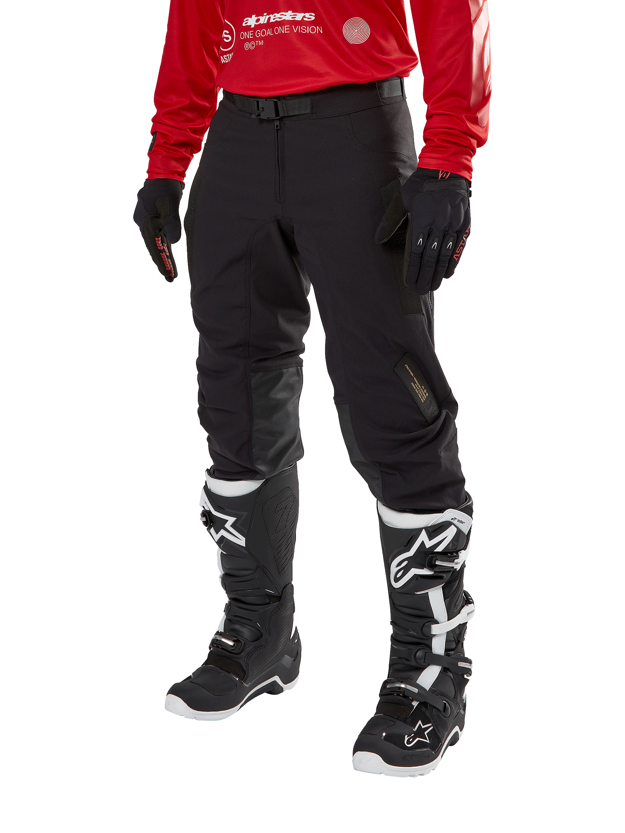 Alpinestars Techdura Pants, pantalon de moto tout-terrain noir, porté avec un maillot rouge à manches longues et des bottes de motocross noires et blanches, doté d'une construction robuste en polyamide extensible, de renforts de genoux internes en cuir et d'une ceinture à boucle réglable pour l'enduro.
