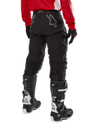 Pantalon Alpinestars Techdura, pantalon d'enduro tout-terrain, noir, vue arrière montrant des logos d'étoile gris sur l'assise, porté avec un maillot rouge à manches longues et des bottes Tech 7 noires et blanches, construction textile robuste pour le pilotage d'aventure