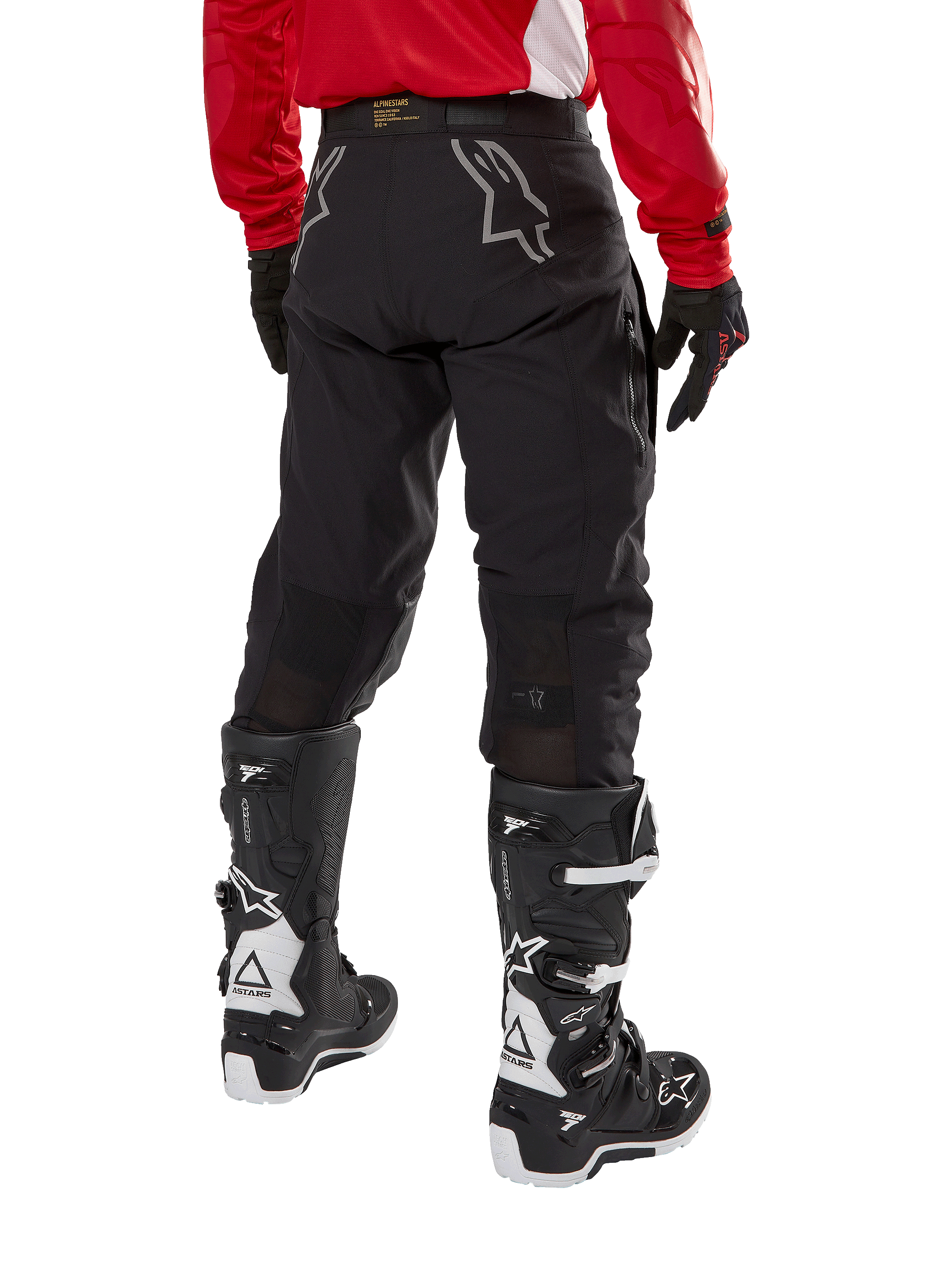 Pantalon Alpinestars Techdura, pantalon d'enduro tout-terrain, noir, vue arrière montrant des logos d'étoile gris sur l'assise, porté avec un maillot rouge à manches longues et des bottes Tech 7 noires et blanches, construction textile robuste pour le pilotage d'aventure