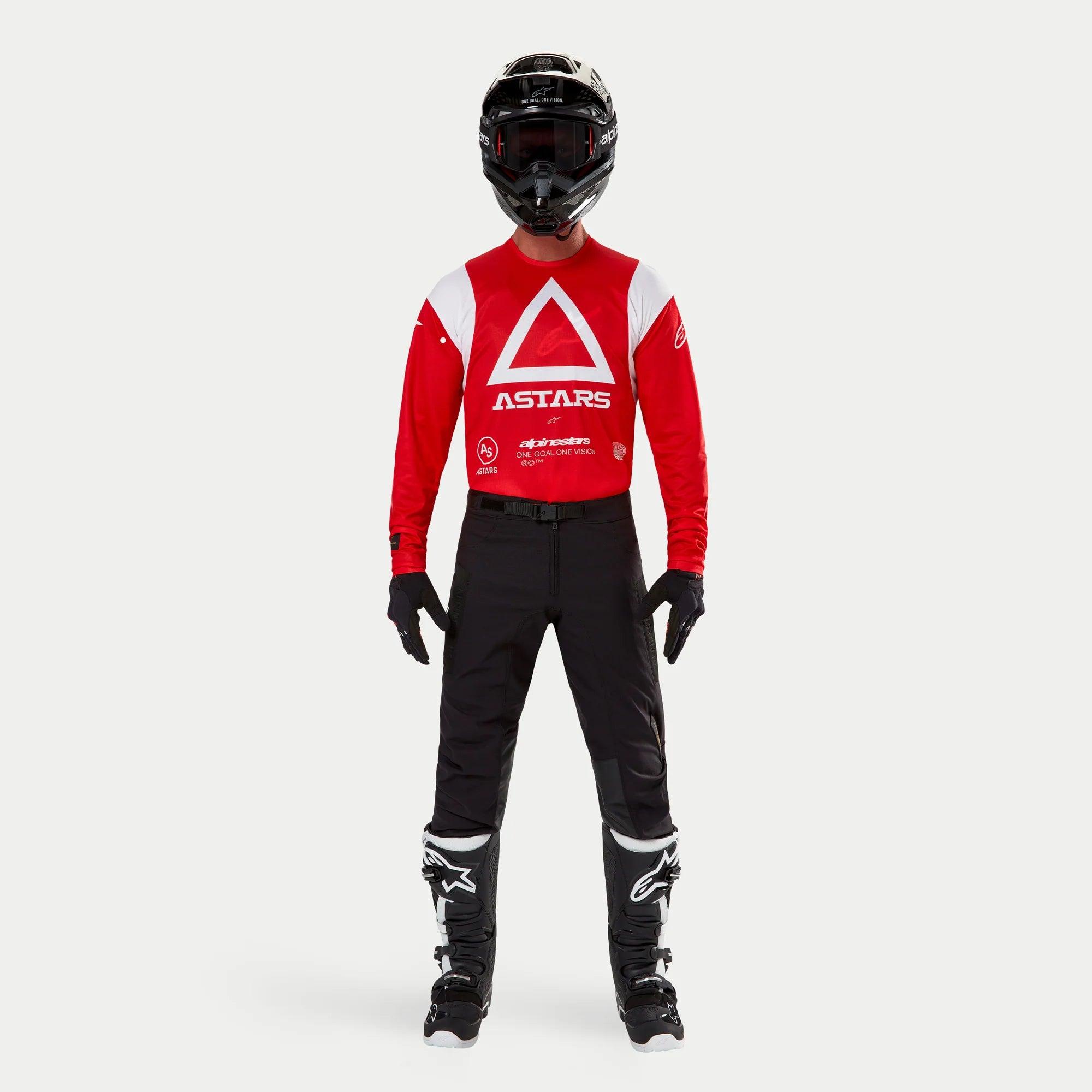 Pantalon Alpinestars Techdura, pantalon d'enduro et de tout-terrain, noir, porté avec un maillot Astars à manches longues rouge et blanc, un casque noir et des bottes noires et blanches, doté d'une construction en polyamide extensible robuste et d'empiècements techniques pour la conduite tout-terrain