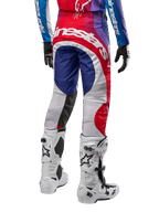 Alpinestars Pantalon Techstar Pneuma 2024, pantalon de motocross, bleu, rouge et blanc, vue arrière porté avec maillot assorti et bottes blanches, logo blanc imposant sur l'assise et empiècements multicolores, équipement de course professionnel