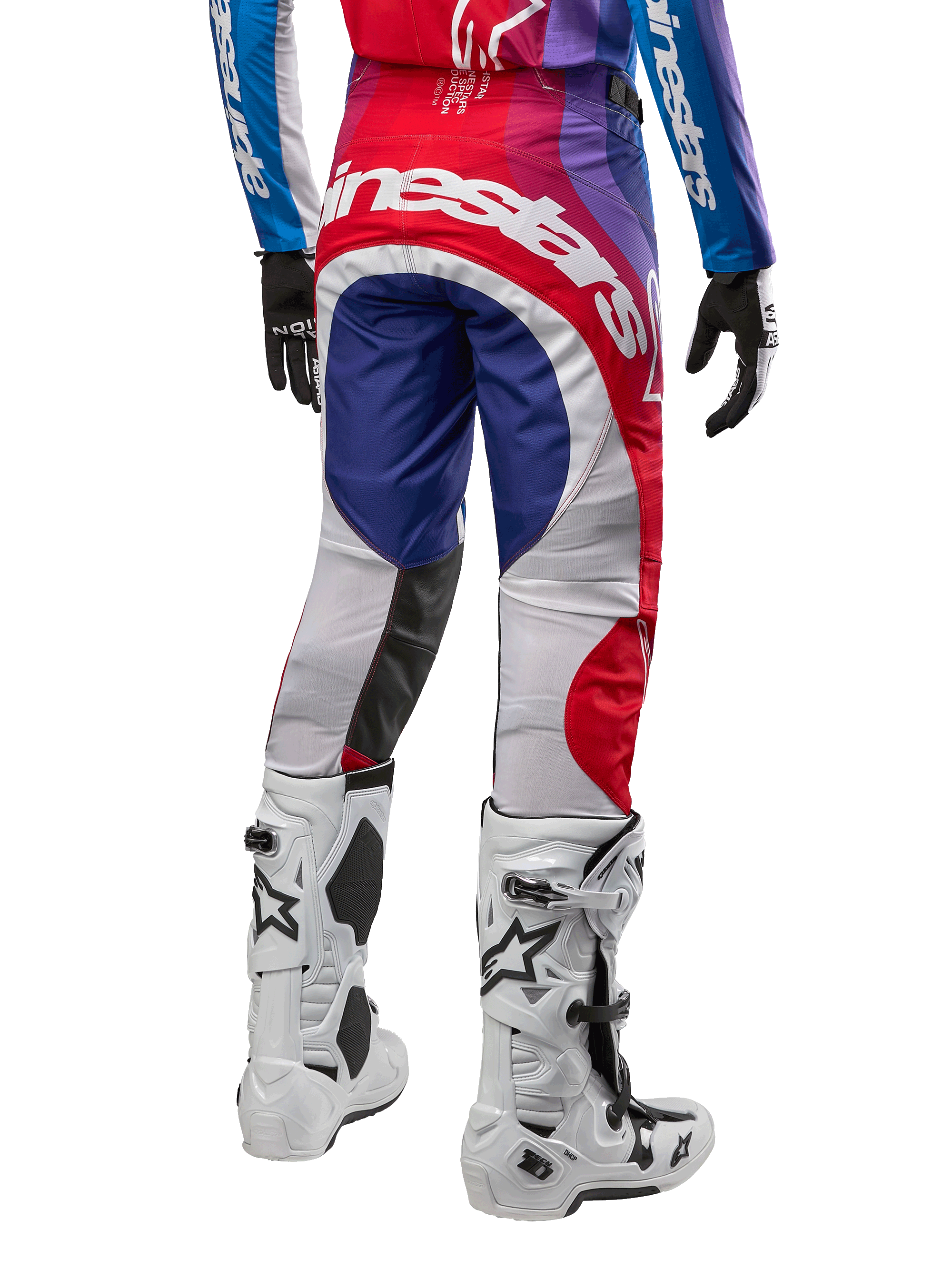 Alpinestars Pantalon Techstar Pneuma 2024, pantalon de motocross, bleu, rouge et blanc, vue arrière porté avec maillot assorti et bottes blanches, logo blanc imposant sur l'assise et empiècements multicolores, équipement de course professionnel