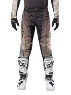 Pantalon Alpinestars Techstar Pneuma 2024, pantalon de motocross, sable foncé et gris poussière de fer, porté avec un maillot assorti, des gants noirs et des bottes blanches et noires, doté de la boucle magnétique SX2 et du marquage Astars, équipement de course tout-terrain durable