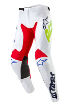 Pantalon Alpinestars Racer Hana 2024, pantalon de motocross, blanc multicolore, avec panneaux intérieurs aux genoux rouges et noirs, logos Astars bleus et marquage jaune néon, conception pré-courbée avec fermeture à cliquet à la taille, équipement textile durable pour la course tout-terrain