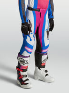Alpinestars pantalon Supertech Maven Junior 2027, pantalon de motocross pour enfant, bleu et corail, conçu pour la compétition tout-terrain, porté avec des bottes de moto.