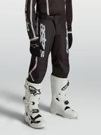 Pantalon Alpinestars Fluid Apex V2 Junior, motocross noir et argenté, coupe ergonomique pré-courbée pour jeunes pilotes.