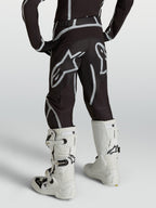 Alpinestars Pantalon Fluid Apex V2 Junior, pantalon de motocross pour enfant, noir et argenté, vue de dos avec bottes blanches