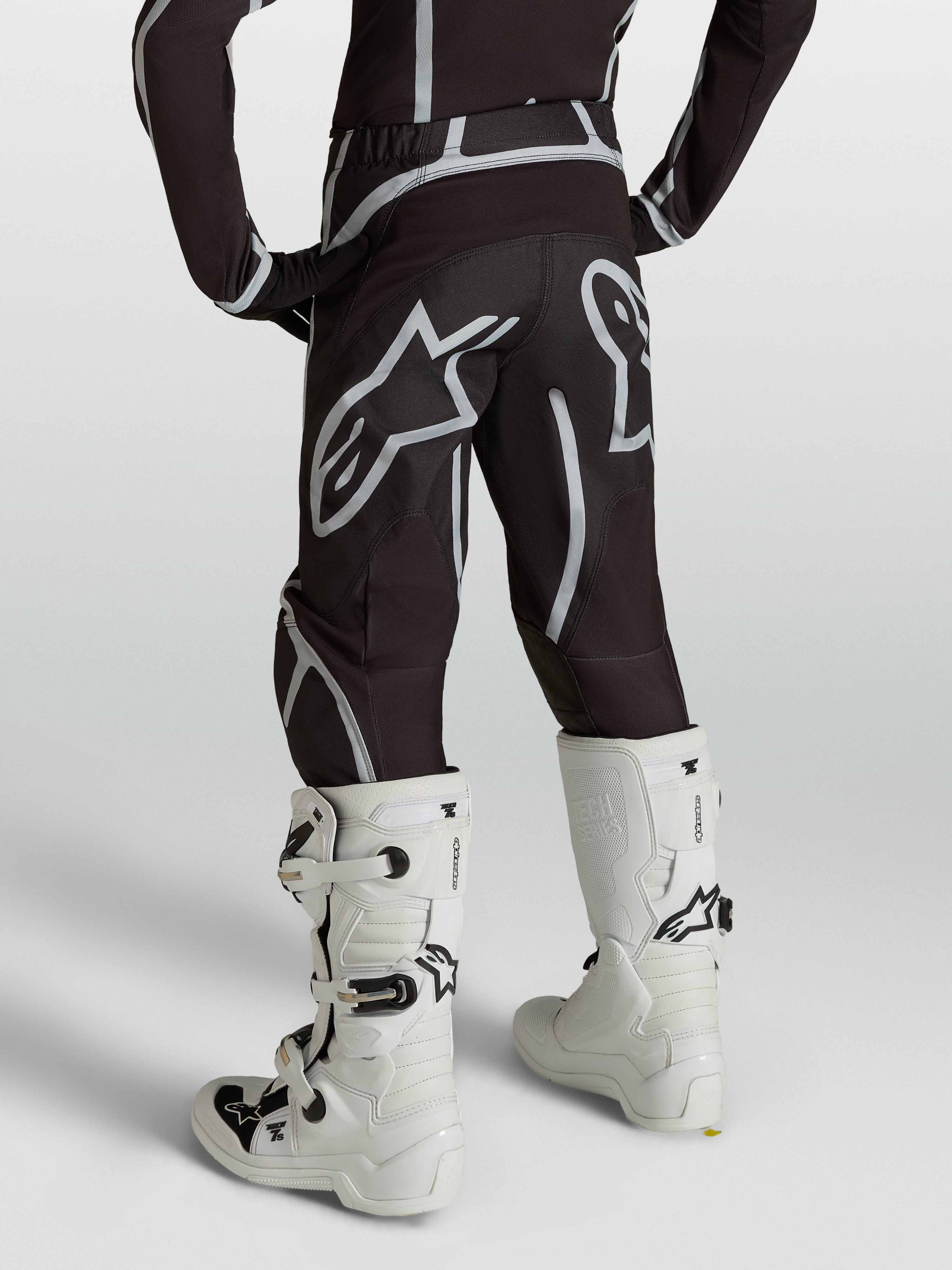 Alpinestars Pantalon Fluid Apex V2 Junior, pantalon de motocross pour enfant, noir et argenté, vue de dos avec bottes blanches