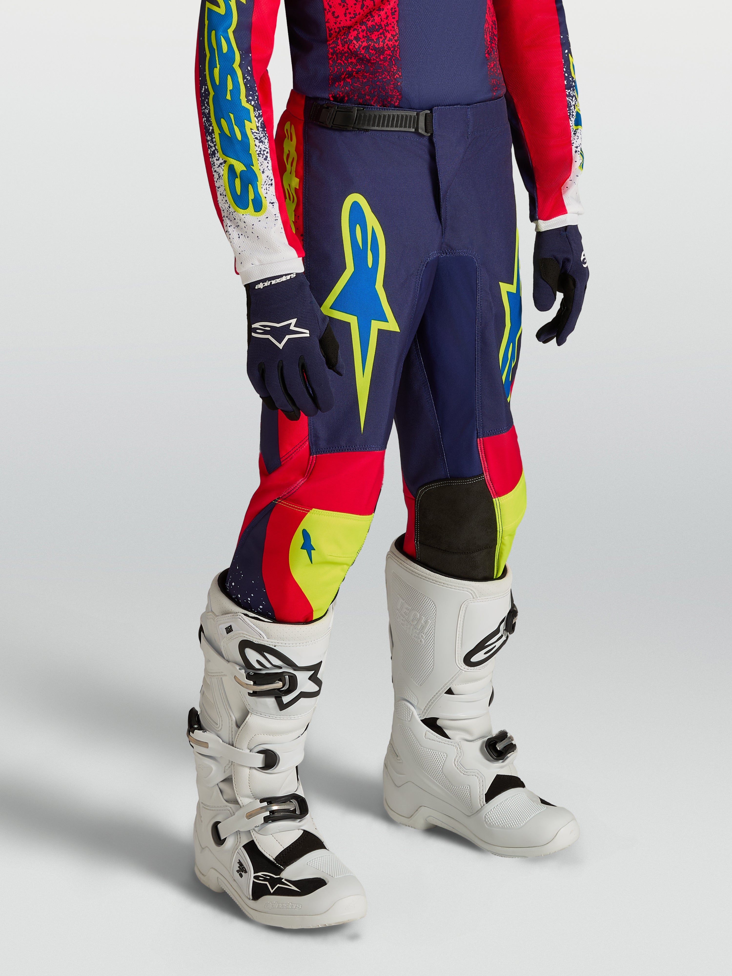 Alpinestars pantalon Fluid Drag Junior 2027, pantalon de motocross bleu marine et rouge avec accents néon et bottes blanches.