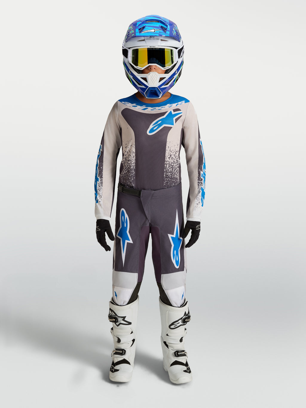 Alpinestars pantalon Fluid Drag Junior 2027, pantalon de motocross pour enfant, gris et bleu, construction durable en polyfibre, porté avec des bottes blanches.