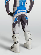 Pantalon Fluid Drag Junior 2027 d'Alpinestars, pantalon de motocross gris et bleu pour enfant, vu de dos avec des bottes de moto blanches.