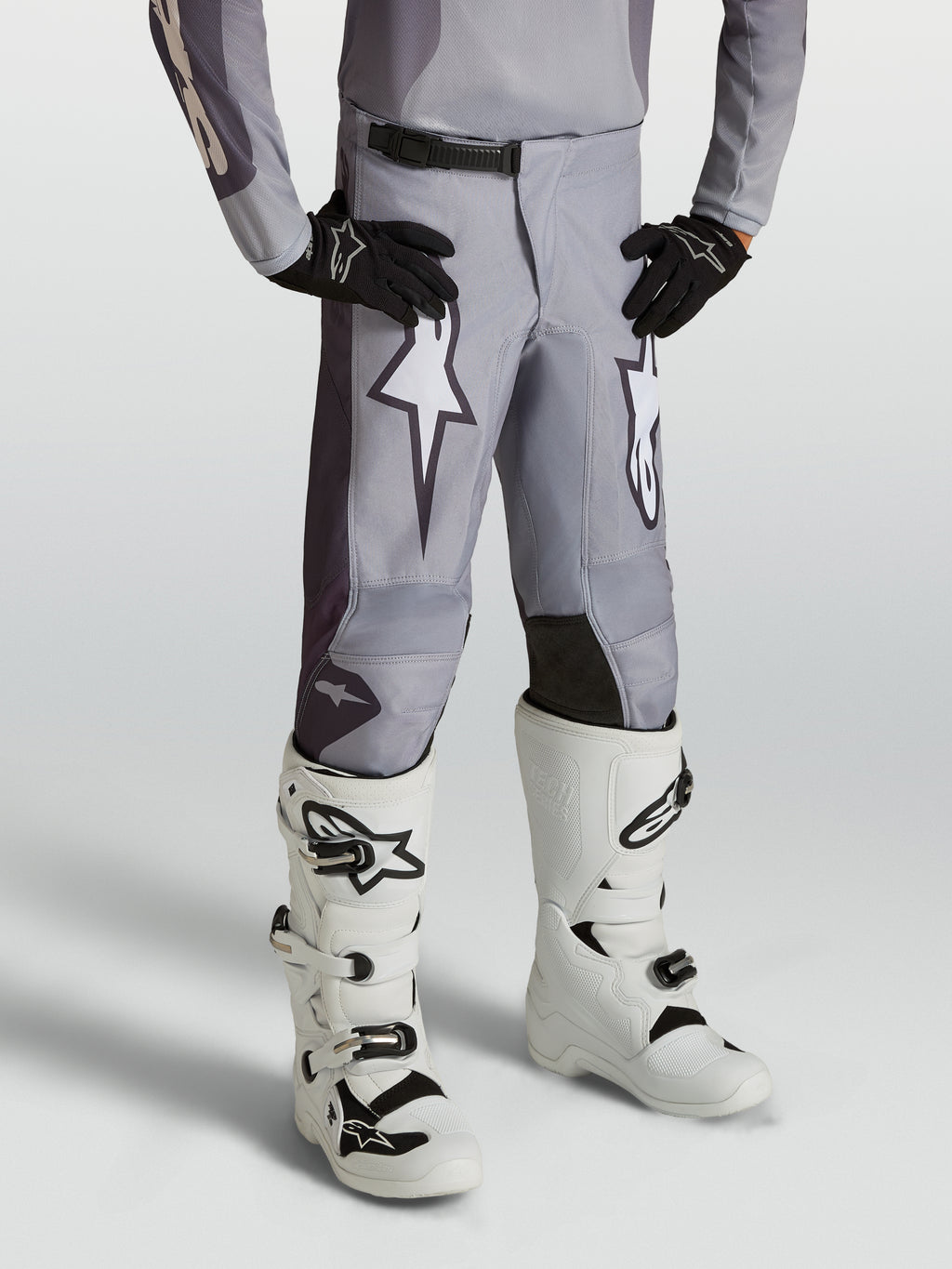 Pantalon Alpinestars Fluid Amber Junior, pantalon de motocross pour junior, gris sable et blanc, avec graphismes d'étoiles et panneaux renforcés, porté par un mannequin.
