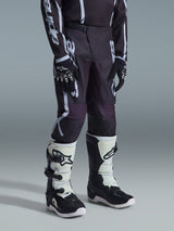 Alpinestars 2026 Youth Fluid Apex Pants, pantalon de motocross, noir et gris avec logo blanc distinctif, porté avec un maillot assorti, des gants noirs et blancs et des bottes blanches et noires, équipement de course tout-terrain professionnel.