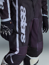Pantalon Alpinestars Youth Fluid Apex 2026, pantalon de motocross, noir et gris, vue en gros plan montrant le logo 'astars' blanc sur la jambe, porté avec des gants et des bottes assortis noir et blanc, design sportif pour les jeunes pilotes de tout-terrain