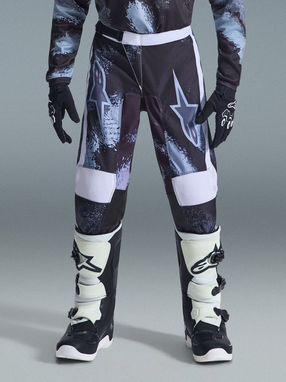 Alpinestars 2026 Youth Fluid Lahnd Pants, Youth Motocross Pants, Iron Camo with white accents, worn with black and white off-road boots and gloves, durable design for young riders.