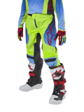 Alpinestars Youth 2024 Racer Hoen Pants, pantalon de motocross pour enfant, jaune fluo et bleu marine avec des accents rouges, porté avec des gants assortis et des bottes blanches, noires et rouges, doté d'une coupe sportive et de jambes pré-courbées pour la course tout-terrain