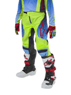 Alpinestars Youth 2024 Racer Hoen Pants, pantalon de motocross pour enfant, jaune fluo et bleu marine avec des accents rouges, porté avec des gants assortis et des bottes blanches, noires et rouges, doté d'une coupe sportive et de jambes pré-courbées pour la course tout-terrain