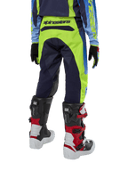 Pantalon Alpinestars Racer Hoen Junior 2024, pantalon de motocross, jaune fluo et bleu marine Night Navy, vue arrière montrant le logo Alpinestars sur la ceinture, porté avec des bottes Tech Series noires et rouges et un maillot assorti, coupe sportive durable pour la conduite tout-terrain des jeunes
