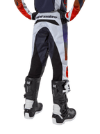 Alpinestars Pantalon Racer Hoen Junior 2024, pantalon de motocross, gris clair avec accents orange vif et noirs, vue arrière présentant des panneaux noirs sur l'assise et les jambes, logo distinctif à la taille, porté avec des bottes de motocross noires et blanches pour la course tout-terrain