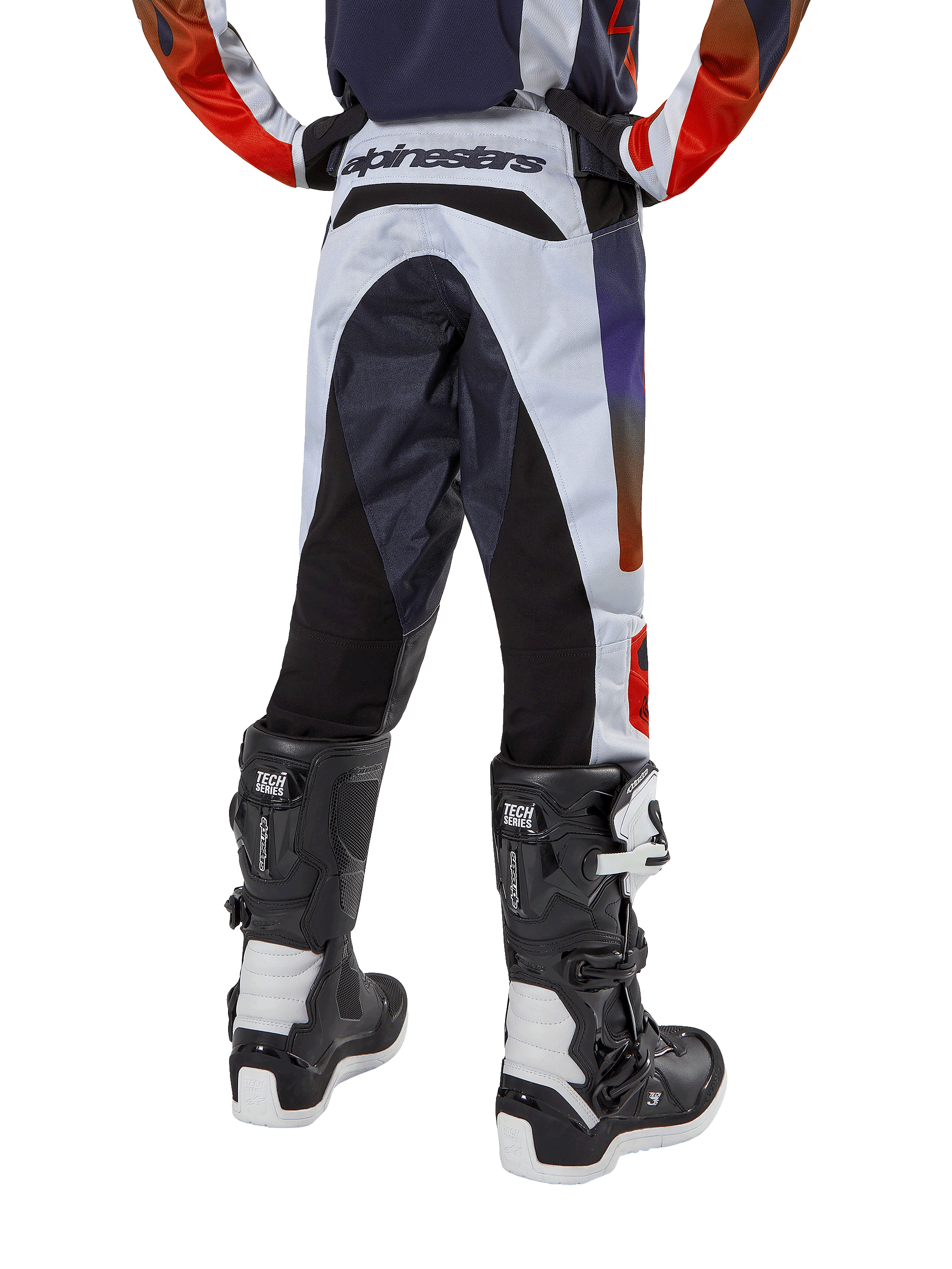 Alpinestars Pantalon Racer Hoen Junior 2024, pantalon de motocross, gris clair avec accents orange vif et noirs, vue arrière présentant des panneaux noirs sur l'assise et les jambes, logo distinctif à la taille, porté avec des bottes de motocross noires et blanches pour la course tout-terrain