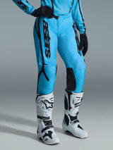 Pantalon Femme Alpinestars Stella Fluid Apex 2026, pantalon de motocross, bleu vif avec logos noirs, porté avec un maillot assorti, des gants noirs et des bottes tout-terrain blanches et noires, conception ergonomique pour la performance