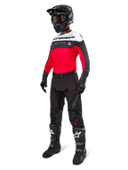 Maillot Alpinestars Pro-Dura, maillot de motocross et d'enduro, noir, rouge vif et blanc, porté avec un pantalon noir, un casque noir et des bottes noires et blanches, doté d'un marquage imposant sur la poitrine et de perforations au laser, équipement haute performance pour la conduite tout-terrain