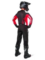 Pilote de motocross vu de dos portant le maillot Alpinestars Pro-Dura noir, rouge vif et blanc, avec pantalon, casque et bottes noirs, montrant le design arrière et les logos sur les manches, équipement de course tout-terrain coordonné