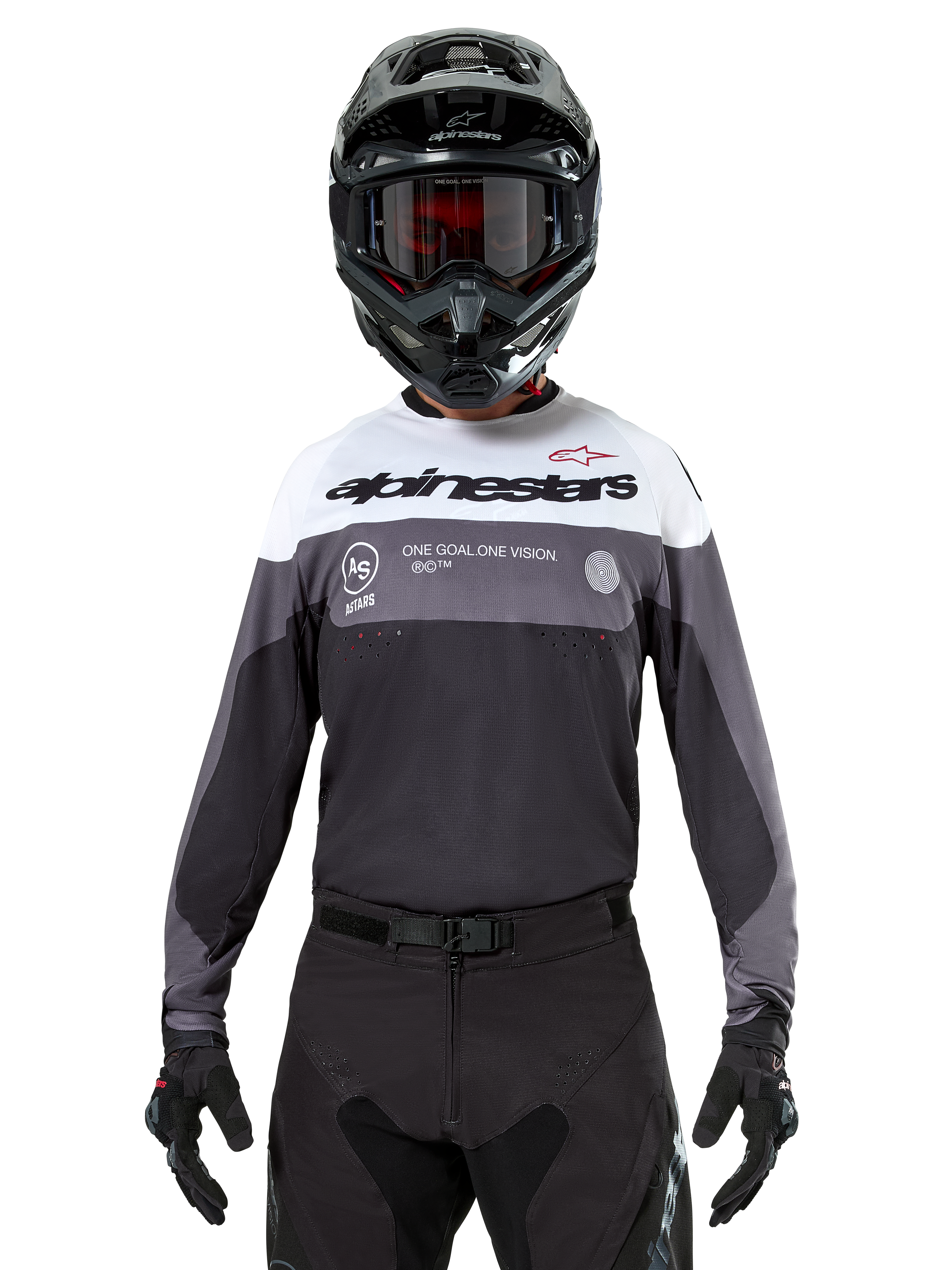 Pilote de motocross portant le maillot Alpinestars Pro-Dura en Black Magnet White, haut de performance à manches longues avec blocs de couleurs blancs et gris, porté avec un casque et des lunettes noirs, arborant le marquage « alpinestars » et le slogan « ONE GOAL ONE VISION », équipement de course de moto tout-terrain