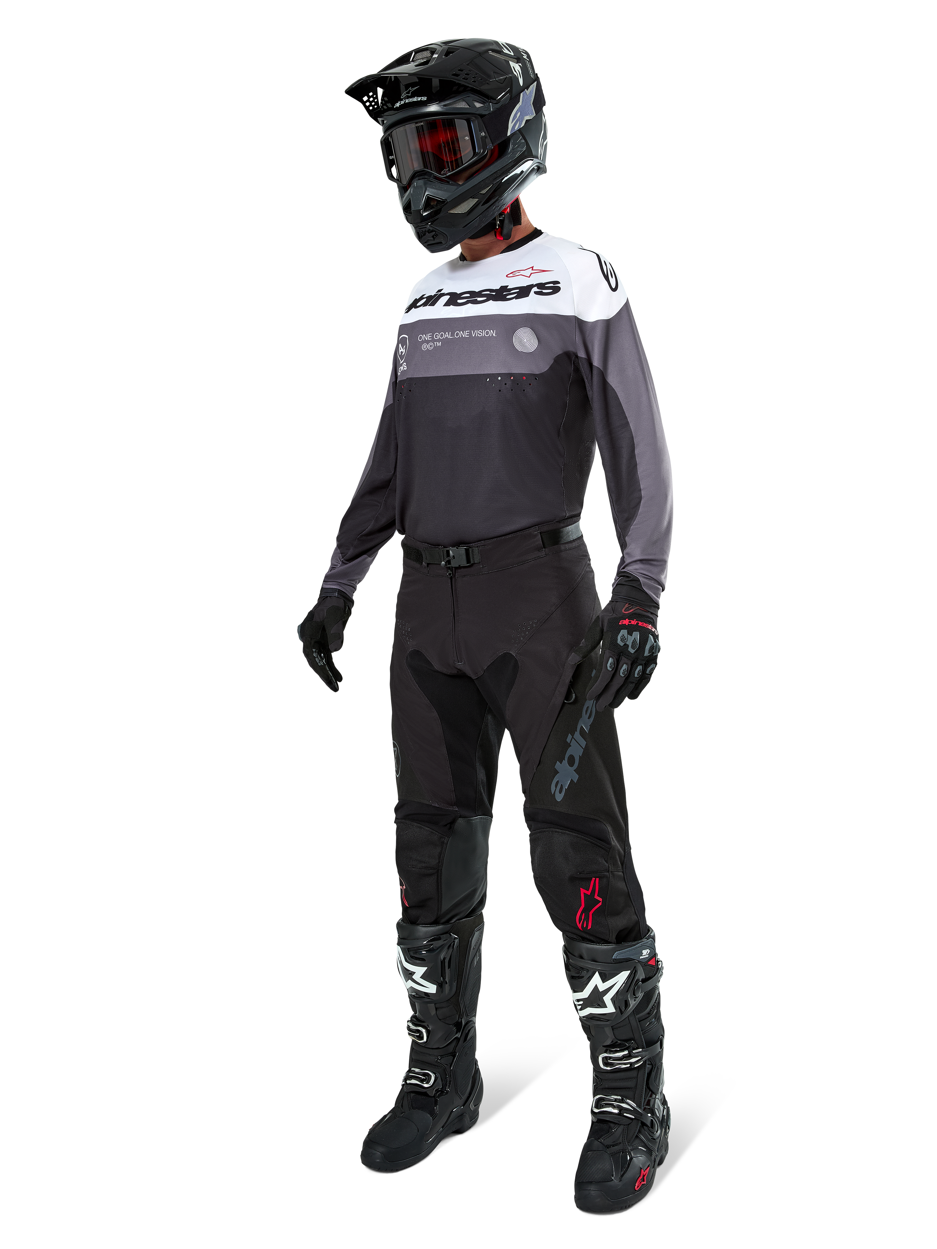 Maillot Alpinestars Pro-Dura en Black Magnet White, porté par un pilote de motocross en tenue complète avec un pantalon noir, un casque noir avec lunettes et des bottes noires et blanches. Le maillot présente un design technique color-block avec des panneaux blancs, gris et noirs, conçu pour la performance en enduro et en tout-terrain.