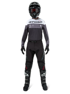 Pilote de motocross portant une tenue de course complète, maillot Pro-Dura en Black Magnet White avec haut de la poitrine blanc et détails gris, associé à un pantalon noir, un casque noir avec lunettes sombres, des bottes noires et blanches, et des gants noirs, ensemble coordonné pour l'enduro et le tout-terrain