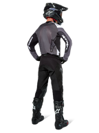 Pilote de motocross portant le maillot Alpinestars Pro-Dura en Black Magnet White, vue arrière montrant le panneau arrière en maille grise et les manches noires avec logo Alpinestars blanc, coordonné avec un pantalon noir, un casque noir et des bottes noires et blanches, équipement de course d'enduro professionnel