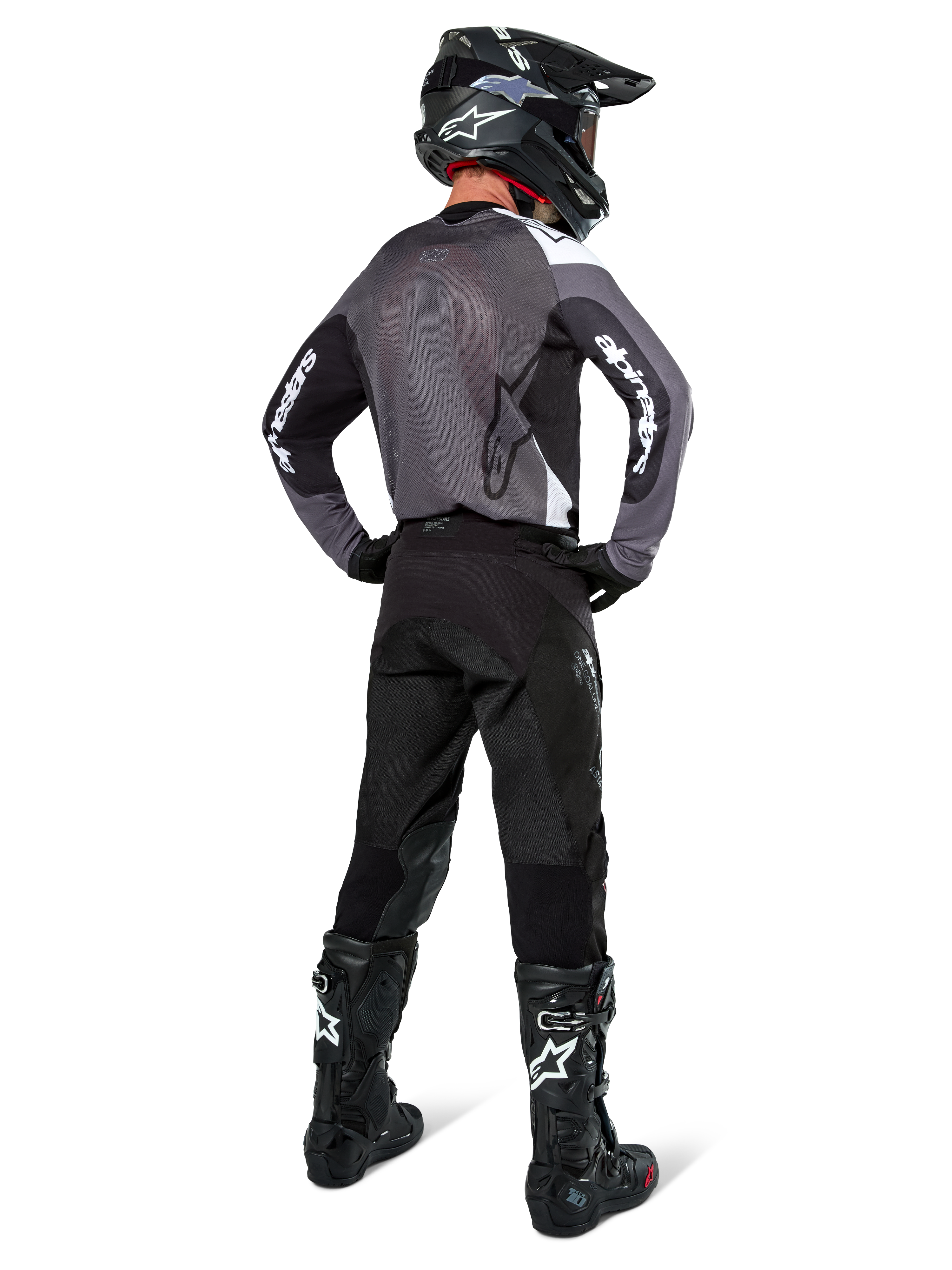 Pilote de motocross portant le maillot Alpinestars Pro-Dura en Black Magnet White, vue arrière montrant le panneau arrière en maille grise et les manches noires avec logo Alpinestars blanc, coordonné avec un pantalon noir, un casque noir et des bottes noires et blanches, équipement de course d'enduro professionnel