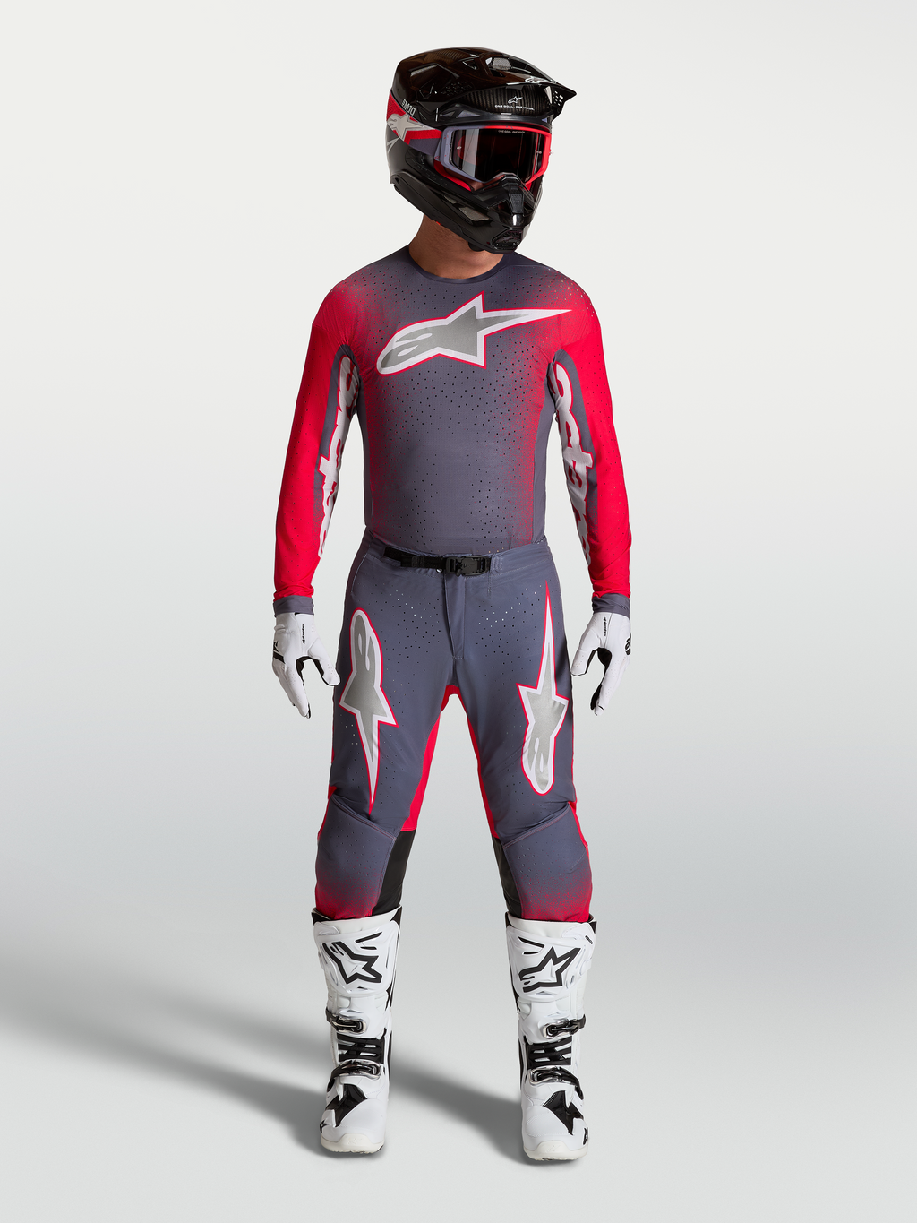 Maillot Alpinestars Supertech Hiten AFD, maillot de motocross pour homme, gris et rouge fluo, coupe athlétique avec mesh ventilé, porté avec équipement complet.