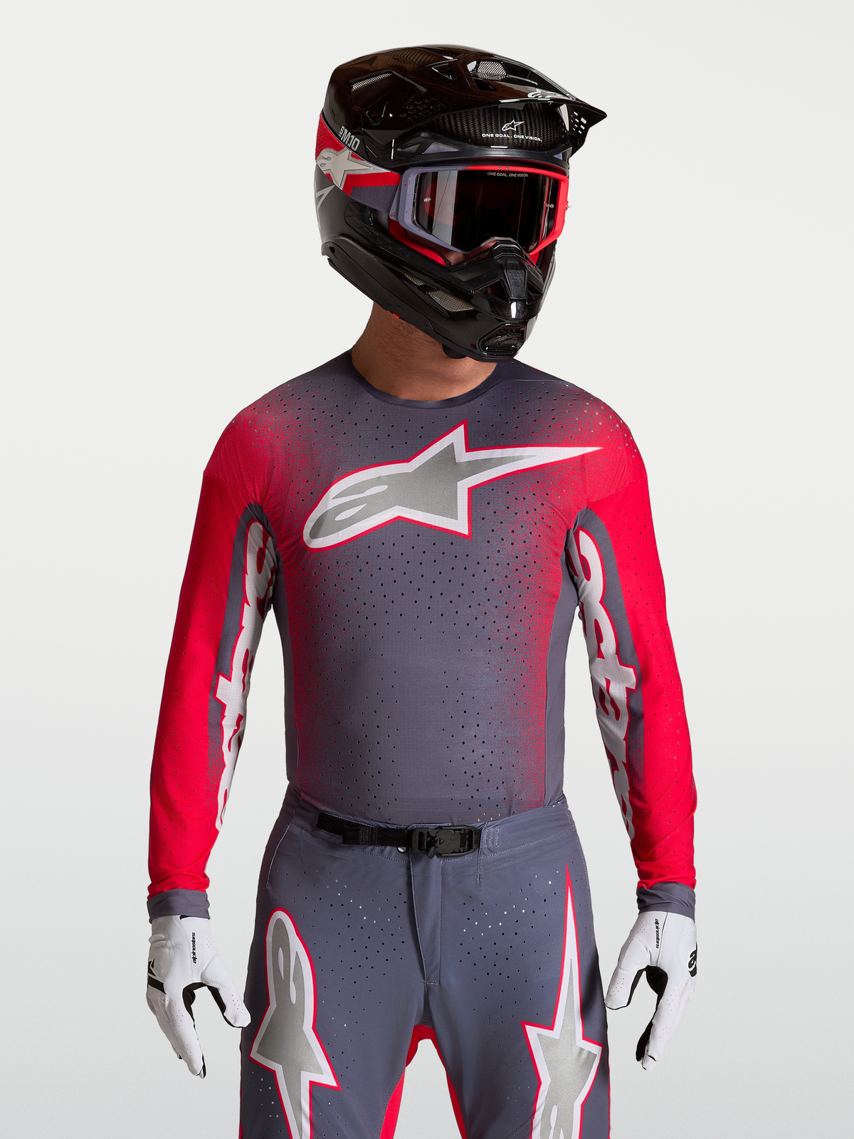 Maillot Alpinestars Supertech Hiten AFD, maillot de motocross pour homme, gris et rouge fluo, mesh ventilé avec perforations au laser, porté par un pilote avec casque et gants.
