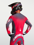 Maillot Supertech Hiten AFD Alpinestars, maillot de motocross gris et rouge fluo, vue de dos montrant la ventilation Stretchnet et la coupe racing athlétique sur un pilote.