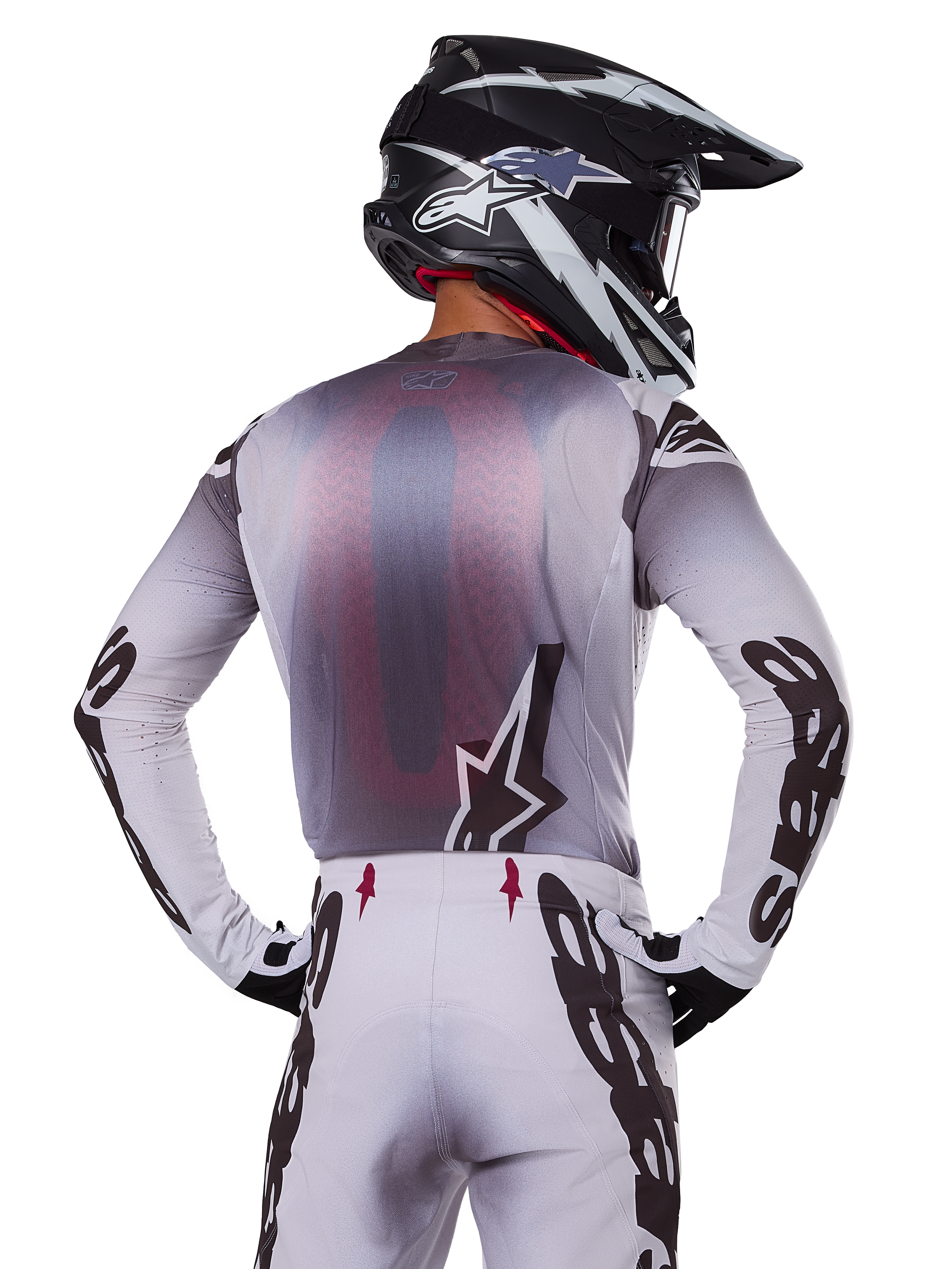 Alpinestars 2025 Supertech Maker Gear Set, motocross rider shown from the back, white and gray jersey with large black branding on sleeves and star logo, matching white pants with black graphics, black and white helmet, professional off-road racing outfit
