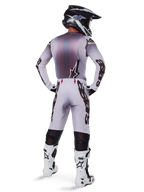 Motocross rider wearing complete racing gear, grey and black jersey, light grey pants with black 'Astars' branding on the sides, black and white helmet, White Tech 10 Boots, coordinated professional off-road racing outfit