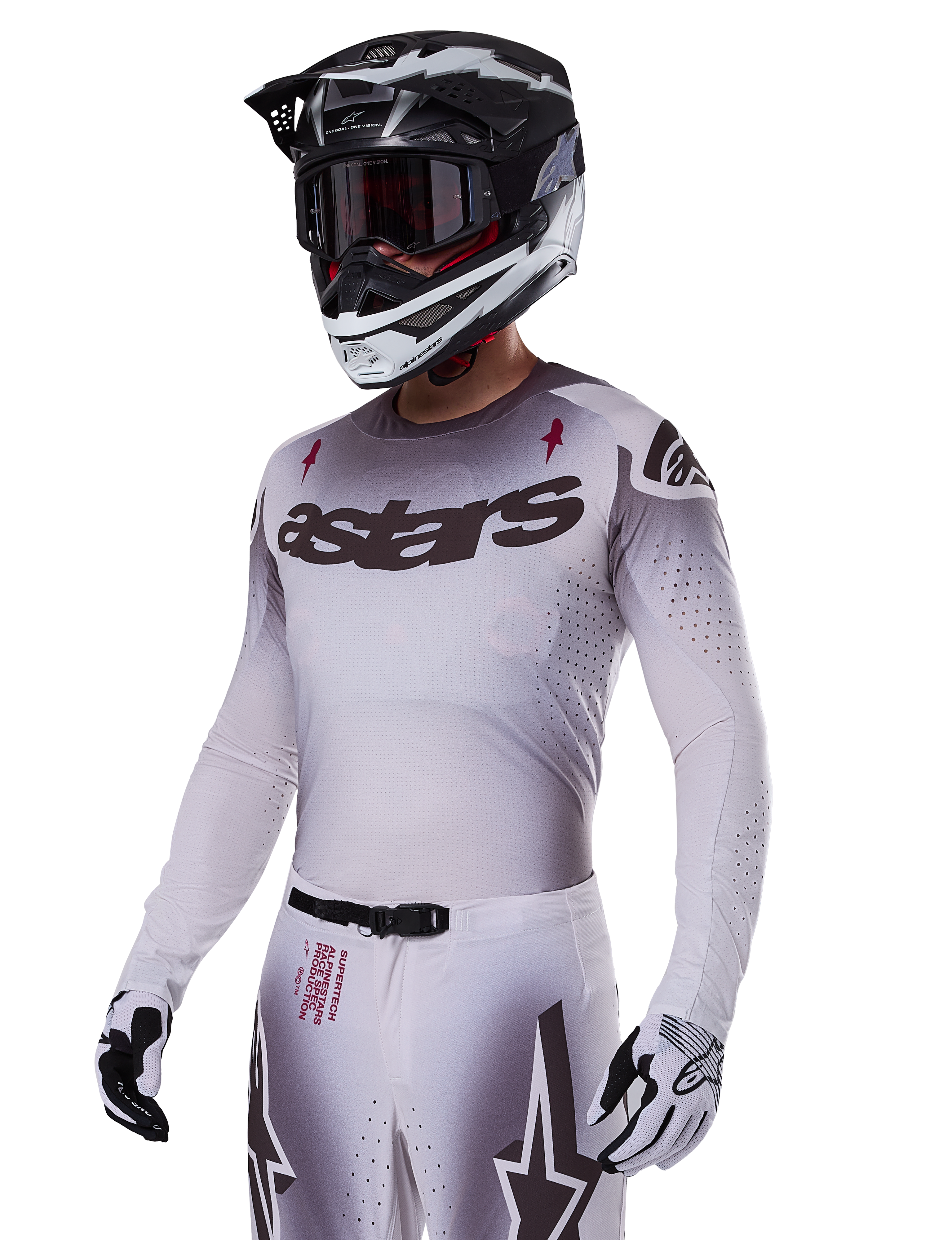 Maillot Alpinestars Supertech Maker 2025, maillot de motocross, dégradé argent et noir, maille extensible respirante avec perforations découpées au laser, porté avec pantalon et casque assortis, avec marquage « astars », équipement tout-terrain professionnel complet