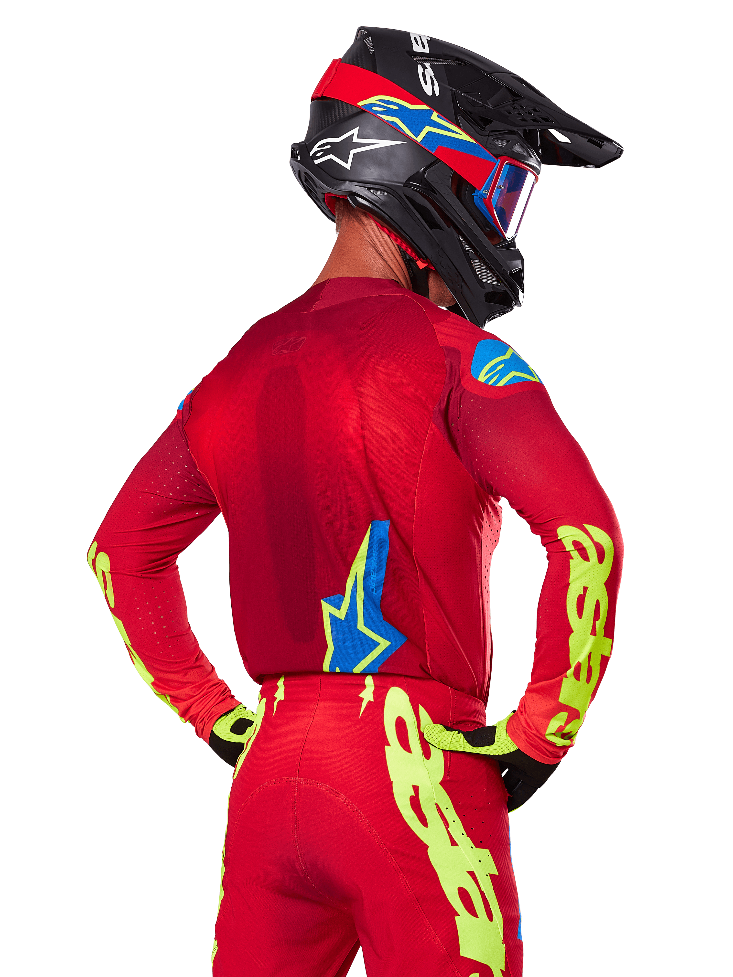 Vue arrière d'un pilote de motocross portant l'ensemble Alpinestars 2025 Supertech Maker rouge, comprenant un maillot rouge avec marquage jaune fluo sur les manches, un pantalon rouge assorti, un casque noir avec des accents bleus et rouges, et des gants noirs et jaunes coordonnés.