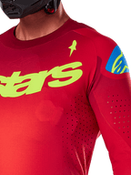 Maillot Alpinestars Supertech Maker 2025, maillot de motocross, rouge vif et jaune fluo, vue rapprochée montrant les perforations découpées au laser, marquage Alpinestars jaune sur la poitrine, détail bleu sur l'épaule, tissu en maille extensible et respirant