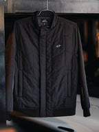 Veste Alpinestars Precedent, veste sportswear matelassée, noire, avec motif matelassé en angle, col bas et fermeture éclair couverte, écusson logo sur la poitrine, poignets et ourlet côtelés, design inspiré du sport automobile