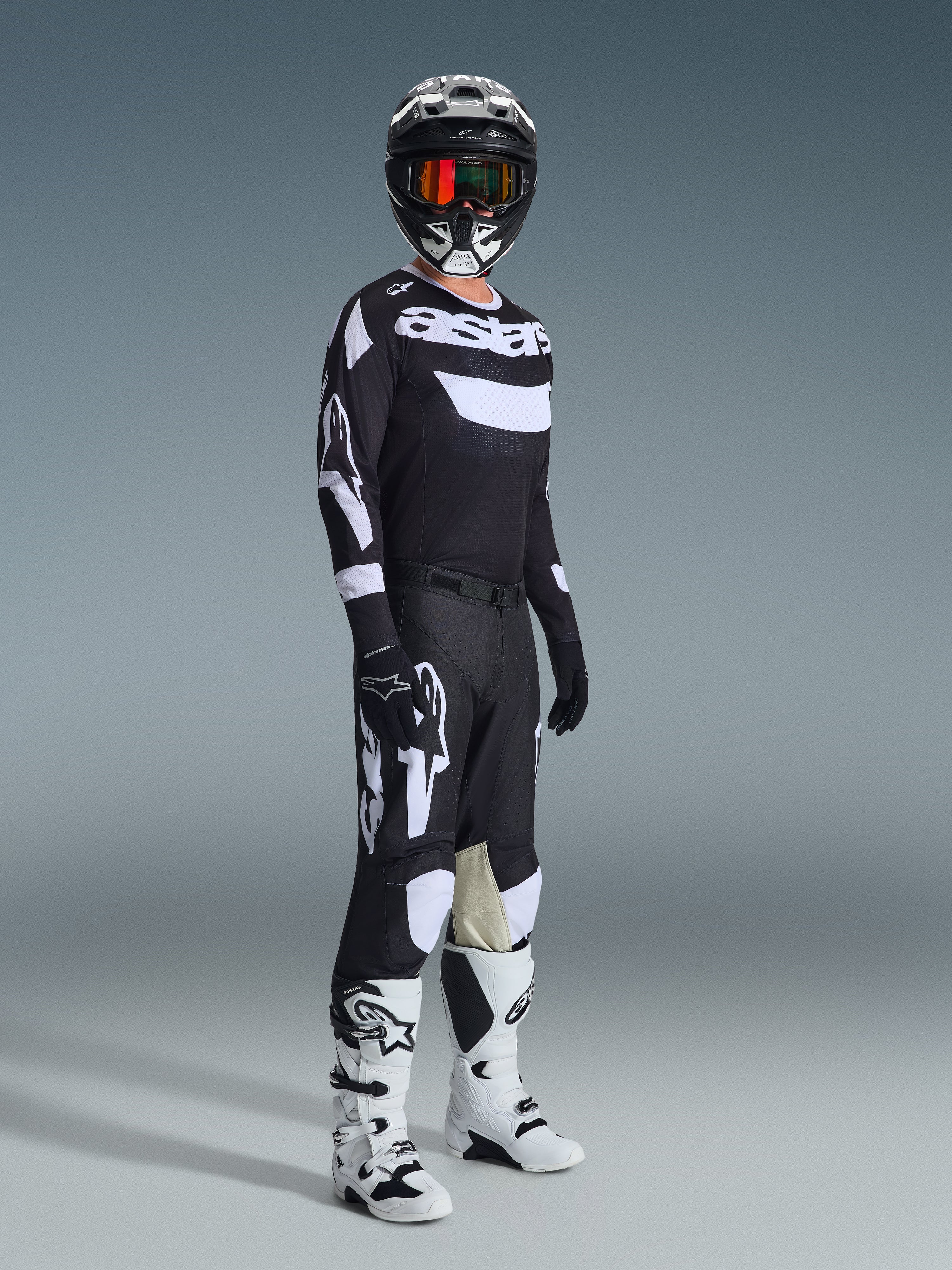 Ensemble d'équipement Alpinestars 2026 Racer Air Riway, pilote de motocross portant une tenue de course complète, maillot noir avec logos 'Astars' blancs et panneaux en mesh, pantalon noir avec grands logos blancs et panneaux aux genoux, casque noir avec lunettes rouges, bottes blanches et noires, tenue de course tout-terrain professionnelle.