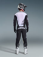 Rear view of a motocross rider wearing the 2026 Racer Air Riway Jersey in Black and White, featuring a breathable mesh back panel, paired with matching black motocross pants with white 'astars' branding, a black and white helmet, and white racing boots.