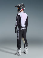 Pilote de motocross vu de dos portant l'ensemble Alpinestars 2026 Racer Air Riway noir et blanc, avec un dos de maillot en maille ventilée et de larges logos blancs, assorti d'un casque noir et de bottes blanches.