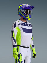 Pilote de motocross portant le maillot Alpinestars Racer Air Riway 2026, gris clair avec des accents jaune fluo et bleu, associé à un casque bleu et jaune assorti et des gants jaune fluo, doté d'une construction en maille respirante et d'un style de course professionnel pour la performance tout-terrain.